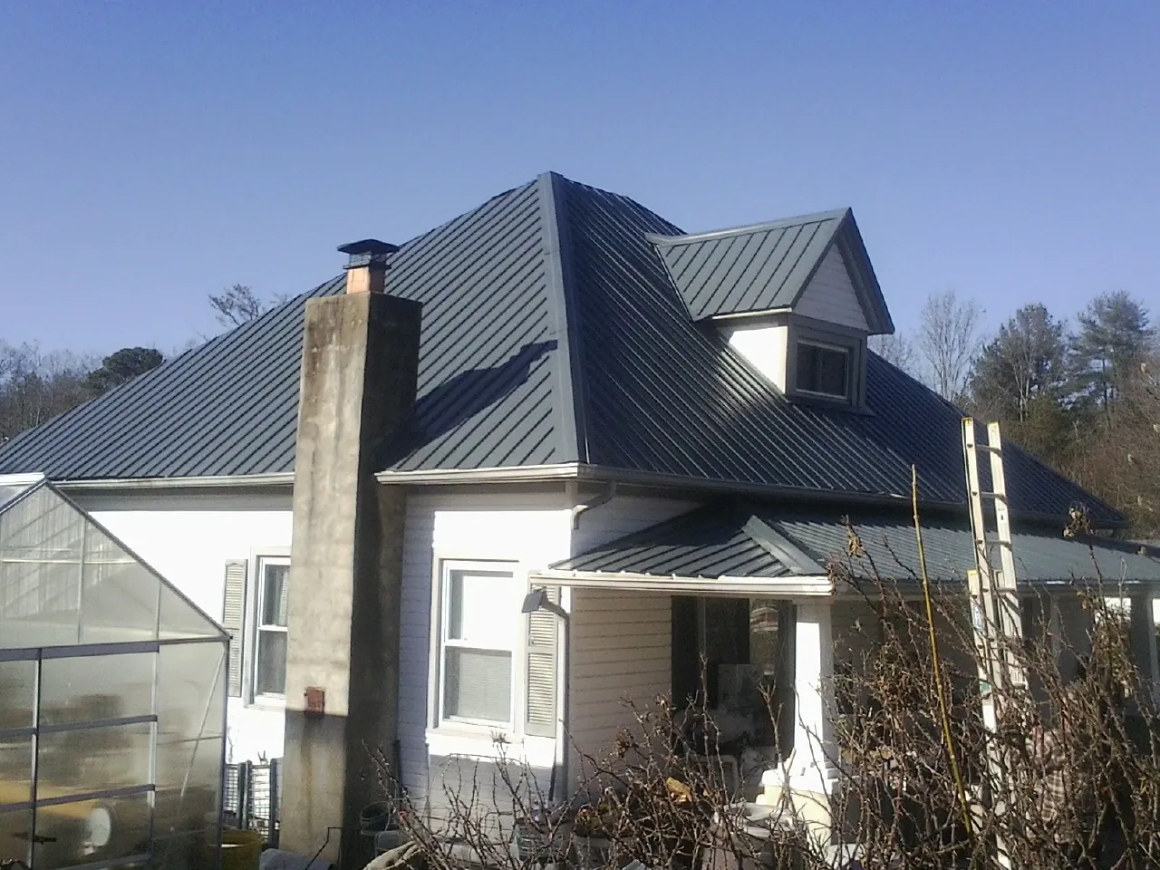Dark blue standing seam metal roof on a white farmhouse with dormer — Slate & Tile Roof Repair by Roofing Brothers in North Falmouth