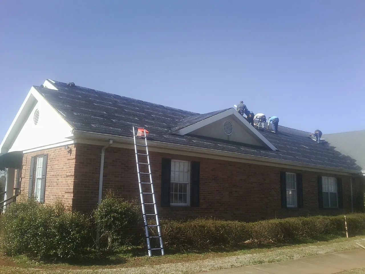 Crew tearing shingles off a brick ranch roof with a ladder set — Metal Roof Repair work by our crew in North Falmouth