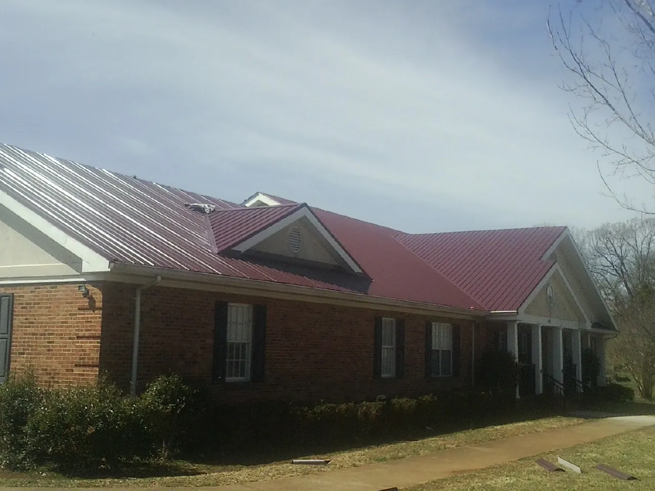 Red metal roof with gabled entries on a long brick building, from a Hail Damage Roof Repair job in North Falmouth