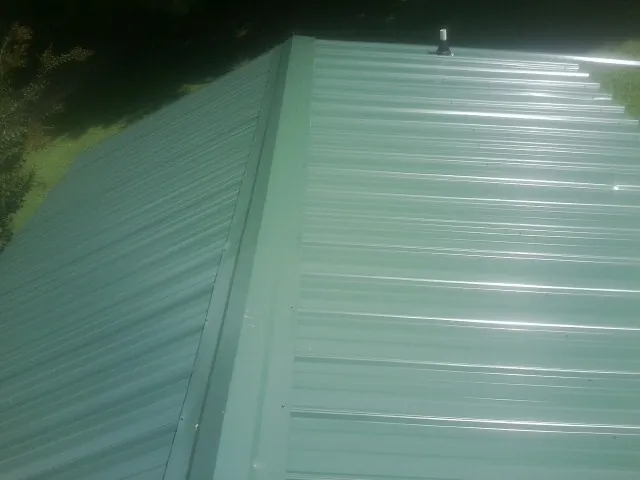 New green metal panels meeting at the ridge of a roof — Flat Roof Repair work by our crew in North Falmouth