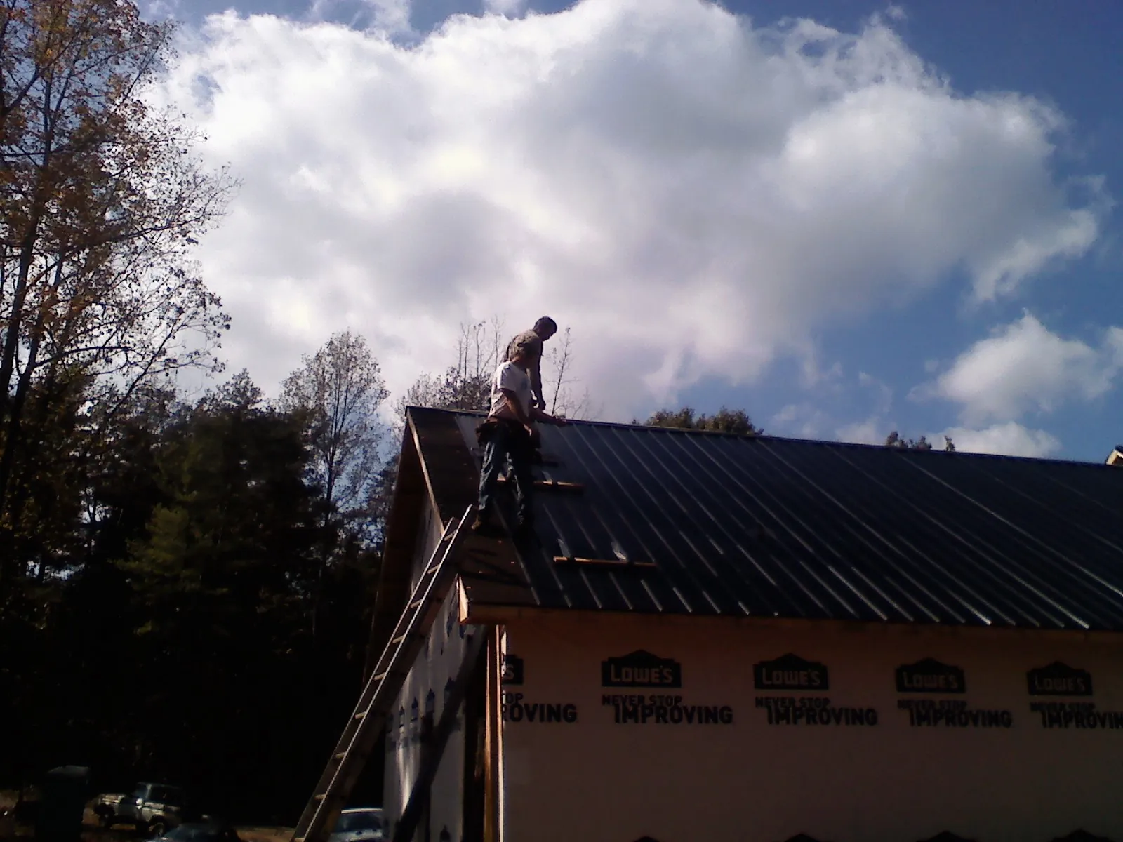 Roofer fastening dark metal panels high against a cloudy sky, from a Roof Inspection job in North Falmouth