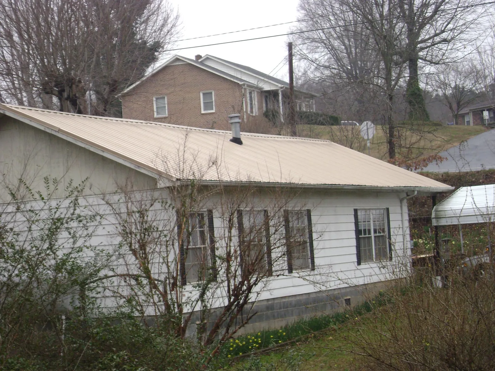 Tan metal roof on a white sided house set into a hillside — Commercial Roofing by Roofing Brothers in North Falmouth