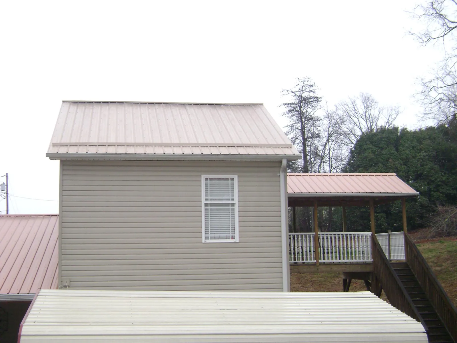 Tan metal roofs on a two story addition and attached porch, from a Roof Replacement job in North Falmouth